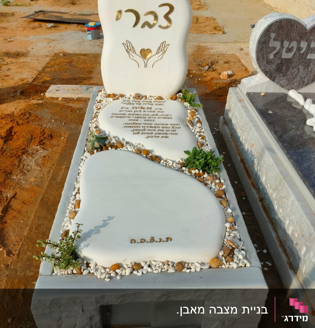 מצבה לבנה עם כיתוב בעברית ועיטור ידיים ולב